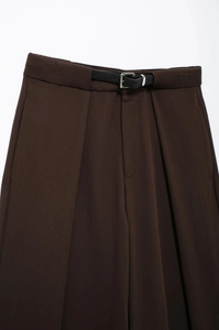 Détail d'un pantalon marron foncé à taille haute avec une fine ceinture en cuir noir et boucle