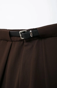 Détail du pantalon marron foncé avec taille plissée et fine ceinture en cuir noir