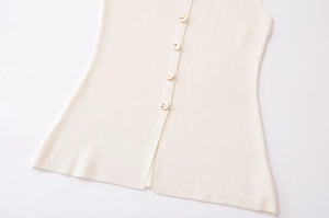 Gros plan sur le gilet en maille crème avec nervures et boutons dorés décoratifs
