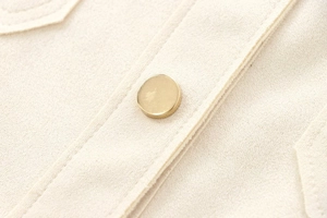 Close-up of golden metal button on premium beige suede texture jacket with fine stitching