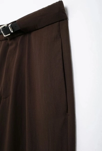 Détail de la taille d'un pantalon marron foncé avec ceinture noire et boucle métallique