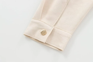 Detailed macro view of apricot suede jacket cuff with a polished gold metal button