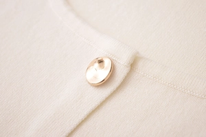 Gros plan d'un bouton métallique doré sur un gilet en maille fine blanc crème
