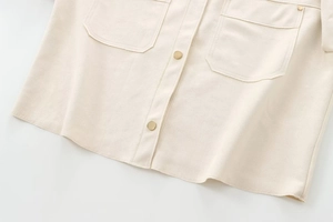 Detailed macro view of beige shacket featuring golden metal buttons and square chest pockets