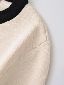 Close-up of contrast black ribbed crew neck and shoulder stitching on cream knit sweater
