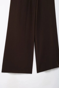 Détail rapproché du pantalon large marron foncé montrant la texture du tissu et l'ourlet