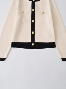 Close-up of cream knit cardigan with black trim and elegant gold embossed buttons