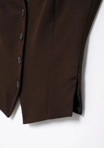 Détail du gilet marron foncé montrant la fente latérale et les quatre boutons en résine
