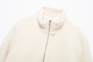 Détail de la texture douce du molleton sherpa et du zip métallique argenté sur la veste crème