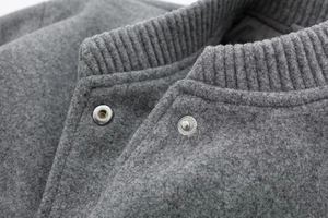 Close-up of gray wool bomber jacket featuring silver snap buttons and ribbed collar detail