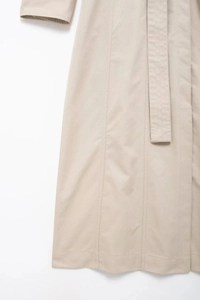 Détail d'un trench-coat beige montrant la texture du tissu, la ceinture et la couture