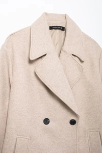 Detail of soft oat-colored wool coat featuring double-breasted buttons and wide lapels