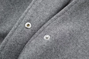 Close-up of silver metal snap button on grey wool blend bomber jacket fabric