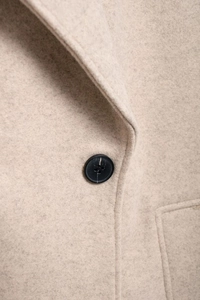 Macro detail of oatmeal wool coat collar featuring a black resin button and fine stitching