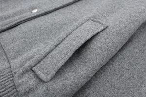 Macro detail of gray wool bomber jacket featuring metallic snap button and ribbed cuff finish