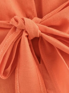 Detail of orange cotton-linen fabric showing tie-up bow design and neat edge stitching