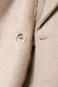 Macro shot of clear round button and soft wool-like texture on oatmeal long coat