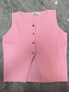 Détail du gilet en maille rose avec des boutons métalliques en forme de cœur sur le devant