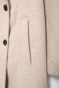 Detail shot of the oatmeal wool blend fabric featuring a pocket and round black button