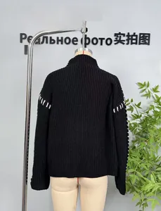 Macro detail of black knit sweater showing white contrast stitching on the sleeves and back
