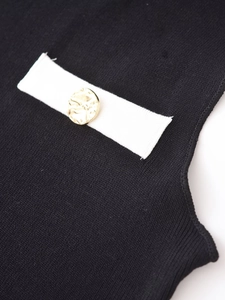 Détail du tricot noir avec bordure blanche et bouton doré texturé sur une robe sans manches
