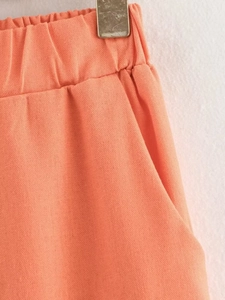 Detailed close-up of elastic waistband and side pockets on orange cotton blend pants