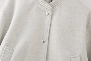 Detail of oatmeal bomber jacket featuring silver metal snap buttons and ribbed knit collar