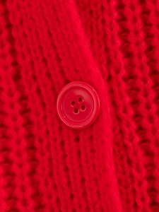 Dettaglio macro di un maglione rosso a maglia con bottone abbinato e trama intrecciata
