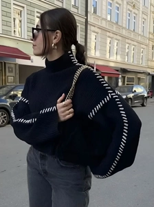 Detail of high neck black knit sweater featuring contrast white whipstitch on shoulders
