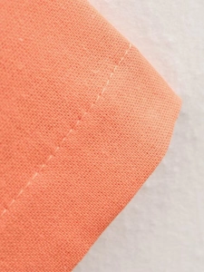 Close-up of coral orange fabric showing detailed twill texture and single-needle stitching