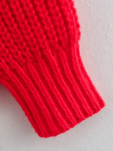 Dettaglio ravvicinato del polsino di un maglione rosso a maglia spessa con trama a costine