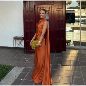 Detail of orange satin backless halter gown featuring a long elegant side cape detail
