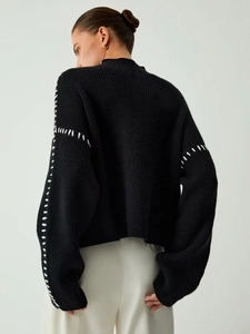 Detail of high-contrast white whipstitch seams on a black knit sweater with drop shoulders