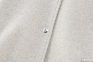 Detailed macro view of soft oatmeal wool fabric with a polished silver metal button