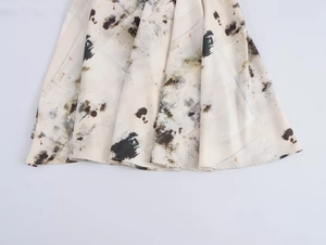 Detailed macro view of flowy cream pleated dress hem with abstract black ink patterns