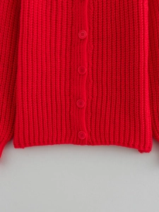 Dettaglio di un cardigan rosso in maglia a coste con trama spessa e bottoni abbinati