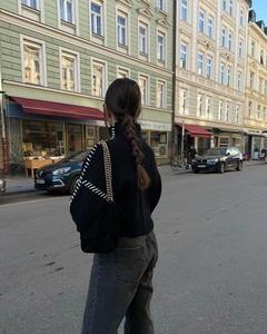 Chic black high-neck knit sweater with contrast white stitching detail in street setting