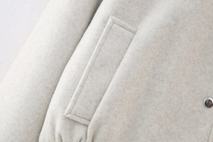 Detailed macro view of light beige wool texture with a silver metal snap button on a jacket