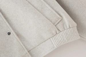 Detail of oatmeal bomber jacket featuring metallic snap button and soft wool blend texture