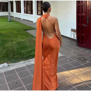 Close-up of an orange satin backless maxi dress with halter ties and a long cape detail
