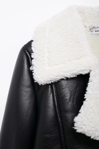 Detail of black faux leather jacket featuring contrast white faux shearling collar