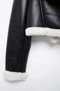 Detail of black faux leather jacket with plush white shearling trim on cuffs and seams