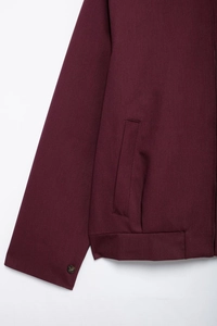 Detail of burgundy zipper jacket showing sleeve buttons and vertical welt pocket design