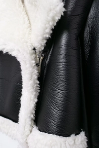 Detailed close-up of premium black leather jacket with white faux shearling collar and zipper