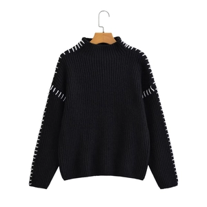 Detail of white whipstitch seams on a black chunky knit high-neck sweater