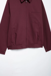 Detail view of burgundy zipper jacket featuring a front pocket and buttoned cuffs