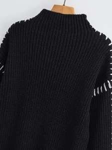 Detail view of black knit sweater featuring contrast white stitching and semi-high collar