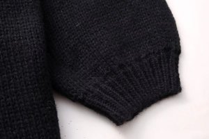 Detailed macro view of the black knitted sweater showing ribbed cuffs and soft texture