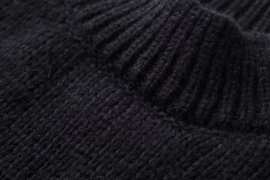 Detailed view of the black knit sweater featuring thick rib-knit texture and neck collar