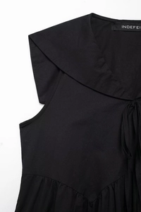 Detail of black dress featuring a sailor collar with tie and pleated waist design
